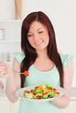 Gorgeous red-haired woman enjoying a mixed salad in the kitchen