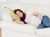 Charming red-haired woman watching tv while lying on a sofa
