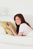 Smiling red-haired female writing a text on her phone while lyin