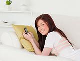 Joyful red-haired female writing a text on her phone while lying