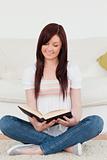 Attractive red-haired woman reading a book while sitting on a so