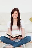 Good looking red-haired woman reading a book while sitting on a 
