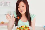 Charming red-haired woman enjoying a mixed salad in the kitchen