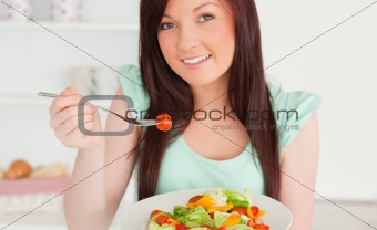 Cute red-haired woman enjoying a mixed salad in the kitchen