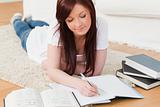 Beautiful joyful red-haired girl studying for while lying on a c