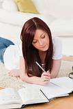 Good looking red-haired girl studying for while lying on a carpe