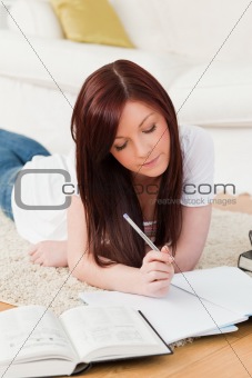 Good looking red-haired girl studying for while lying on a carpe