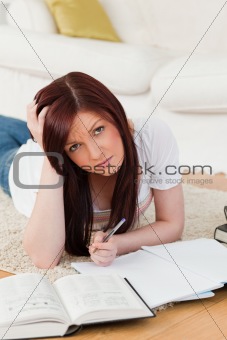 Beautiful red-haired female studying for while lying on a carpet