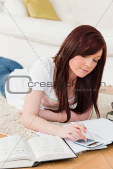 Cute red-haired girl studying for while lying on a carpet