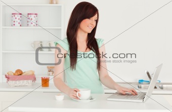 Beautiful red-haired female relaxing with her laptop in the kitc