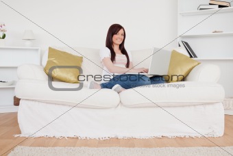 Cute red-haired woman relaxing with her laptop while sitting on 