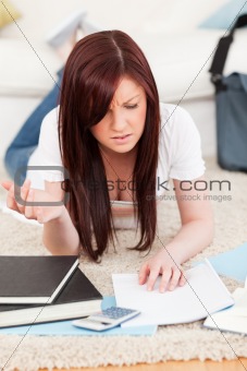 Upset red-haired female studying for while lying on a carpet