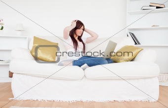 Beautiful red-haired female being depressed after gambling with her laptop while sitting on a sofa