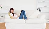 Attractive red-haired woman reading a book while lying on a sofa