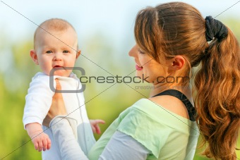 Smiling mother holding surprised baby in hands at summer day
