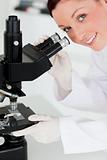Charming red-haired scientist looking through a microscope