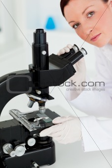 Cute red-haired scientist looking through a microscope