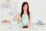 Pretty red-haired woman cutting some cake in the kitchen