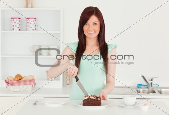 Attractive red-haired woman cutting some cake in the kitchen