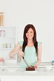 Beautiful red-haired woman cutting some cake in the kitchen
