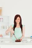 Good looking red-haired woman cutting some cake in the kitchen