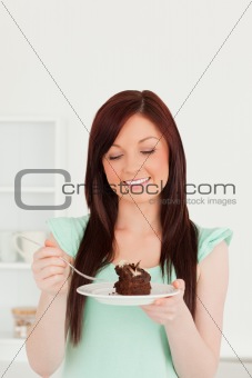 Attractive red-haired woman eating some cake in the kitchen