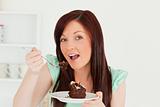 Charming red-haired woman eating some cake in the kitchen