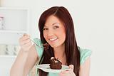 Cute red-haired woman eating some cake in the kitchen