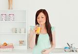 Attractive red-haired woman enjoying a glass of orange juice in 
