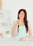 Smiling red-haired woman enjoying a glass of orange juice in the