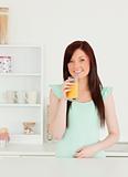 Joyful red-haired woman enjoying a glass of orange juice in the 