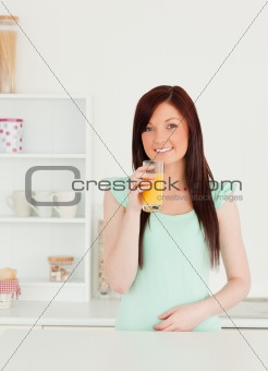 Joyful red-haired woman enjoying a glass of orange juice in the 