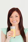 Cheerful red-haired woman enjoying a glass of orange juice in th