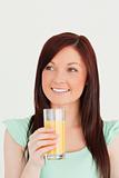 Glad red-haired woman enjoying a glass of orange juice in the ki