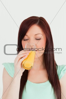 Attractive red-haired woman drinking a glass of orange juice in 