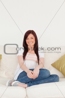 Attractive red-haired woman posing while sitting on a sofa in th