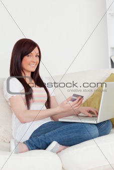 Attractive woman sitting on a sofa is going to make a payment on