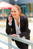 Smiling business woman leaning on railing and talking on mobile
