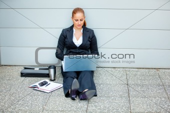 Pensive business woman sitting on floor at office building  and using laptop

