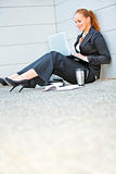 Smiling business woman sitting on floor at office building  and using laptop
