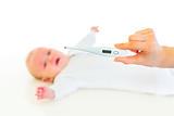 Woman's hand holding thermometer and crying baby laying on back  in background

