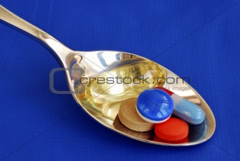 A spoonful of medicine including painkiller and vitamin isolated on blue