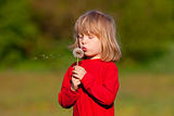 boy with long blond hair holding dandelion standing in a field