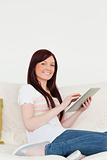 Attractive red-haired woman relaxing with her tablet while sitti