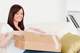 Attractive red-haired woman opening a carboard box while sitting