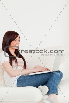 Smiling red-haired woman relaxing with her laptop while sitting 