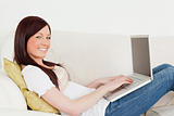 Beautiful red-haired woman relaxing with her laptop while lying 