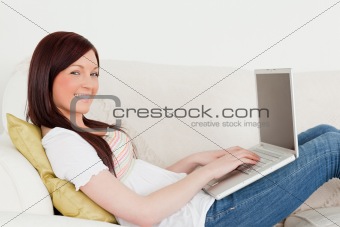 Beautiful red-haired woman relaxing with her laptop while lying 