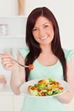 Attractive red-haired woman enjoying a mixed salad in the kitche