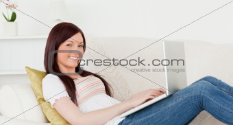 Attractive red-haired woman relaxing with her laptop while lying